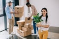 young woman holding potted plant and smiling at camera while male colleagues holding boxes behind Royalty Free Stock Photo