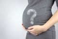 Young woman holding pregnant belly in hands with hologram question mark. Pregnancy, maternity concept. Close-up, copy space Royalty Free Stock Photo