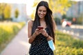 Young woman holding protective face mask while using smart phone and text messaging in the street Royalty Free Stock Photo