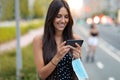 Young woman holding protective face mask while using smart phone and text messaging in the street Royalty Free Stock Photo