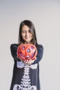 young woman holding a pumpkin and making a wink face. Wearing a black and white skeleton costume. Halloween concept. Indoors.