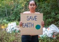 The young woman holding `Save The Earth` Poster showing a sign protesting against plastic pollution in the forest. The concept of Royalty Free Stock Photo