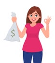 Young woman holding/showing cash, money, currency note bag with dollar sign and gesturing or making okay/OK sign with hand fingers Royalty Free Stock Photo