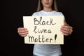 Young woman holding sign with phrase Black Lives Matter on dark background, closeup. Racism concept