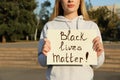 Young woman holding sign with phrase Black Lives Matter outdoors, closeup. Racism concept