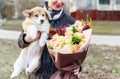 A young woman is holding a small, cute funny dog and a beautiful bouquet of flowers Royalty Free Stock Photo