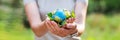 Young woman holding small planet in hands against spring or summer green background. Ecology, environment and Earth day Royalty Free Stock Photo