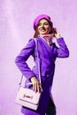 Young woman holding stylish handbag and wearing trendy purple coat. Spring female clothes and accessories. Fashion