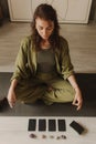 Young Woman holding Tarot cards and sitting in lotus pose on yoga mat, relaxed with closed eyes. Mindful meditation concept.