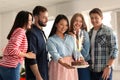 Young woman holding tasty cake with firework candles and her friends at birthday party indoors Royalty Free Stock Photo