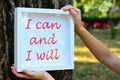 Young woman holding by a tree , a framed motivational message stating I can and I will