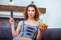 Young woman holding TV remote control in one hand and a bowl of popcorn in another is looking very surprised Royalty Free Stock Photo