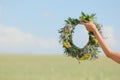 Young woman holding wreath made of beautiful flowers in field on sunny day, closeup Royalty Free Stock Photo