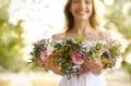 Young woman holding wreath made of beautiful flowers outdoors, focus on hands Royalty Free Stock Photo
