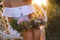 Young woman holding wreath made of flowers on swing chair outdoors at sunset, closeup Royalty Free Stock Photo