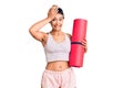 Young woman holding yoga mat stressed and frustrated with hand on head, surprised and angry face Royalty Free Stock Photo