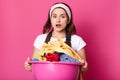 Young woman holds basin full of clean linen, housewife looks tired after doing laundry, works about house, dresses brown apron,