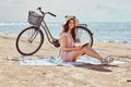 Young woman holds a book and looking at camera while sitting on the beach. Royalty Free Stock Photo