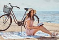 Young woman holds a book and looking at camera while sitting on the beach. Royalty Free Stock Photo