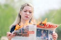 A young woman holds a burning newspaper. Portrait of a young woman looking at a burning newspaper. A burning newspaper in a woman