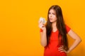 A young woman holds a 1 dollar banknote and looks perplexed, a concept of small income. Studio photo on a yellow background.