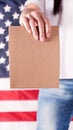 Young woman holds empty cardboard with Space for Text sign against American flag on background. Girl protesting anti-abortion laws