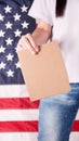 Young woman holds empty cardboard with Space for Text sign against American flag on background. Girl protesting anti-abortion laws