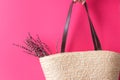 Young woman holds in hand woven beach straw wicker bag with leather handles with bouquet of lavender flowers on fuchsia pink wall