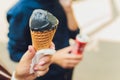 Young woman holds in hands dark black cone ice-cream. Close-up portrait female with red lips. Black waffle horn. Trendy