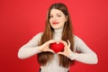 A young woman holds a heart in her hands on a red background, a blood donor. Valentine's Day