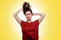 A young woman holds her hair in a knot with her hands. Yellow background. Copy space. Hair care concept