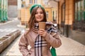 Young woman holds hot warming drink in her hands and walks through the city streets Royalty Free Stock Photo