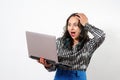 A young woman holds a laptop in her hand, emotionally clutching her head with her hand. on white background