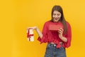 Young woman holds an open gift box and looks admiringly into it. Girl received gift on yellow background