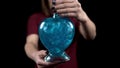 A young woman holds out a bottle with a love potion in the camera. Glass bottle in the form of a heart with blue liquid