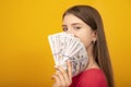 Young woman holds a stack of dollar bills fanned near her face against a bright yellow orange background. Copy space Royalty Free Stock Photo