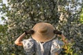 Young woman holds straw hat with her hands in black vintage lace gloves. Back view. Spring blossom apple tree garden. Royalty Free Stock Photo