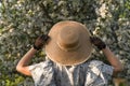 Young woman holds straw hat with her hands in black vintage lace gloves. Back view. Spring blossom apple tree garden. Royalty Free Stock Photo