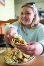 Young woman holds up a tasty taco at a Mexican restaurant, showing her delicious dinner. Woman is intentionally defocused to focus