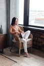 Young woman at home sitting on chair relaxing in her living room reading book Royalty Free Stock Photo