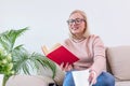 Young woman at home sitting on modern sofa relaxing in her living room reading book and drinking coffee or tea. White cozy bed and Royalty Free Stock Photo