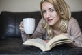 Young woman at home sitting near window relaxing in her living room reading book and drinking Royalty Free Stock Photo