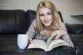 Young woman at home sitting near window relaxing in her living room reading book and drinking Royalty Free Stock Photo