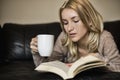 Young woman at home sitting near window relaxing in her living room reading book and drinking Royalty Free Stock Photo