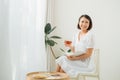 Young woman at home sitting near window relaxing in her living room reading book and drinking tea Royalty Free Stock Photo