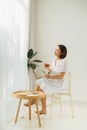 Young woman at home sitting near window relaxing in her living room reading book and drinking tea Royalty Free Stock Photo