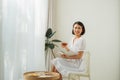 Young woman at home sitting near window relaxing in her living room reading book and drinking tea Royalty Free Stock Photo