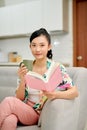 Young woman at home sitting on sofa relaxing in her living room reading book and drinking coffee Royalty Free Stock Photo