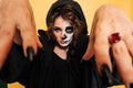A young woman in a hood with scary makeup. on a yellow isolated background. She& x27;s terrifying with her hands. Concert