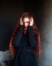 Young woman in horrible dark room on background of black wall, portrait of frightened and desperate girl